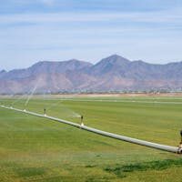 Wide view of a green field being irrigated, with mountains in the background under a clear sky.